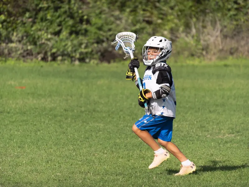 A young lacrosse player with a stick and ball at a backyard practice setup.