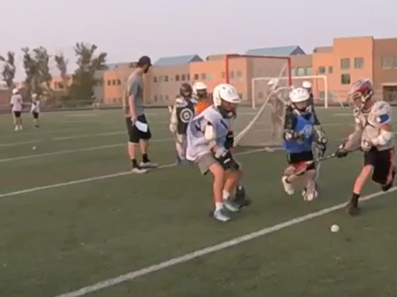 Youth lacrosse players in a full-field game with a coach on the sideline in San Antonio