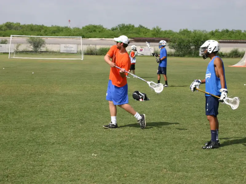 Coach working with two young lacrosse players on the field in San Antonio