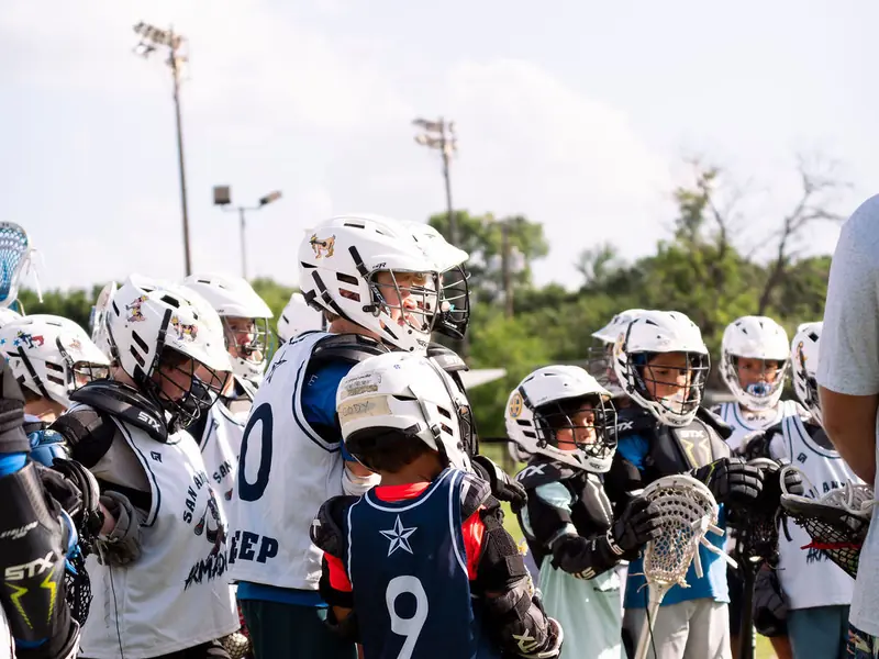 Young lacrosse players and their coach on the sideline at a San Antonio clinic